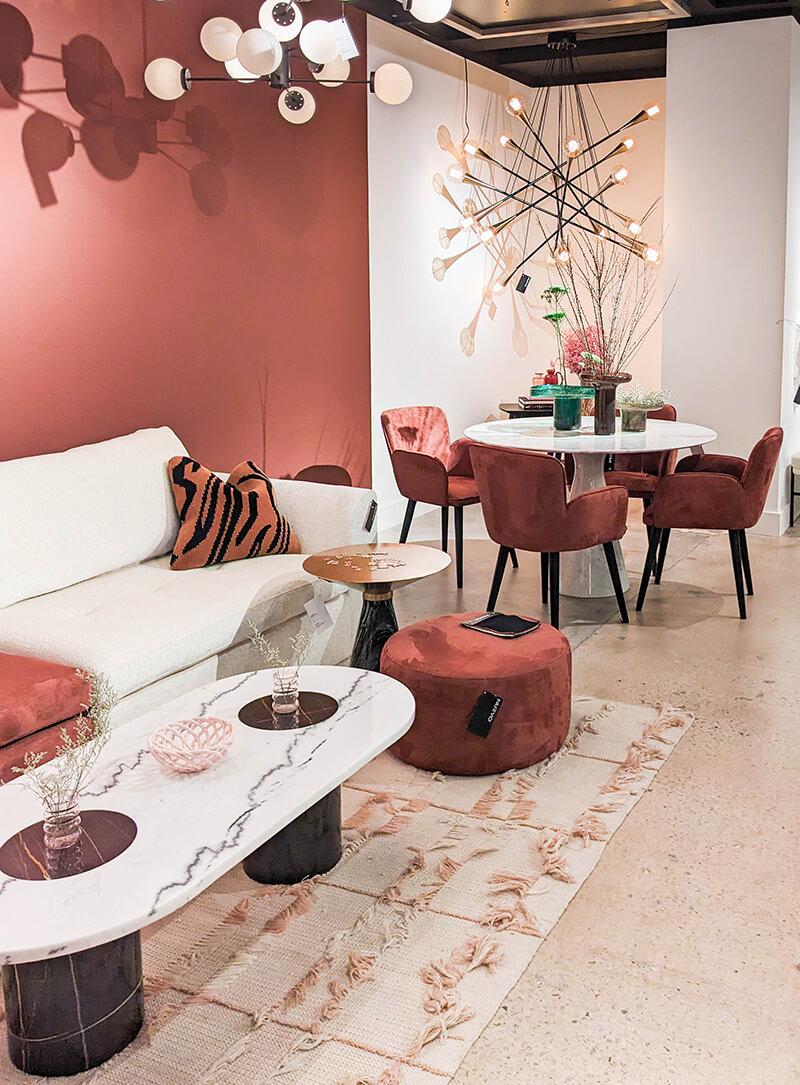 A cream sofa with a rose ottoman next to a dining table with rose dining chairs in front of a wall painted in cream and rose